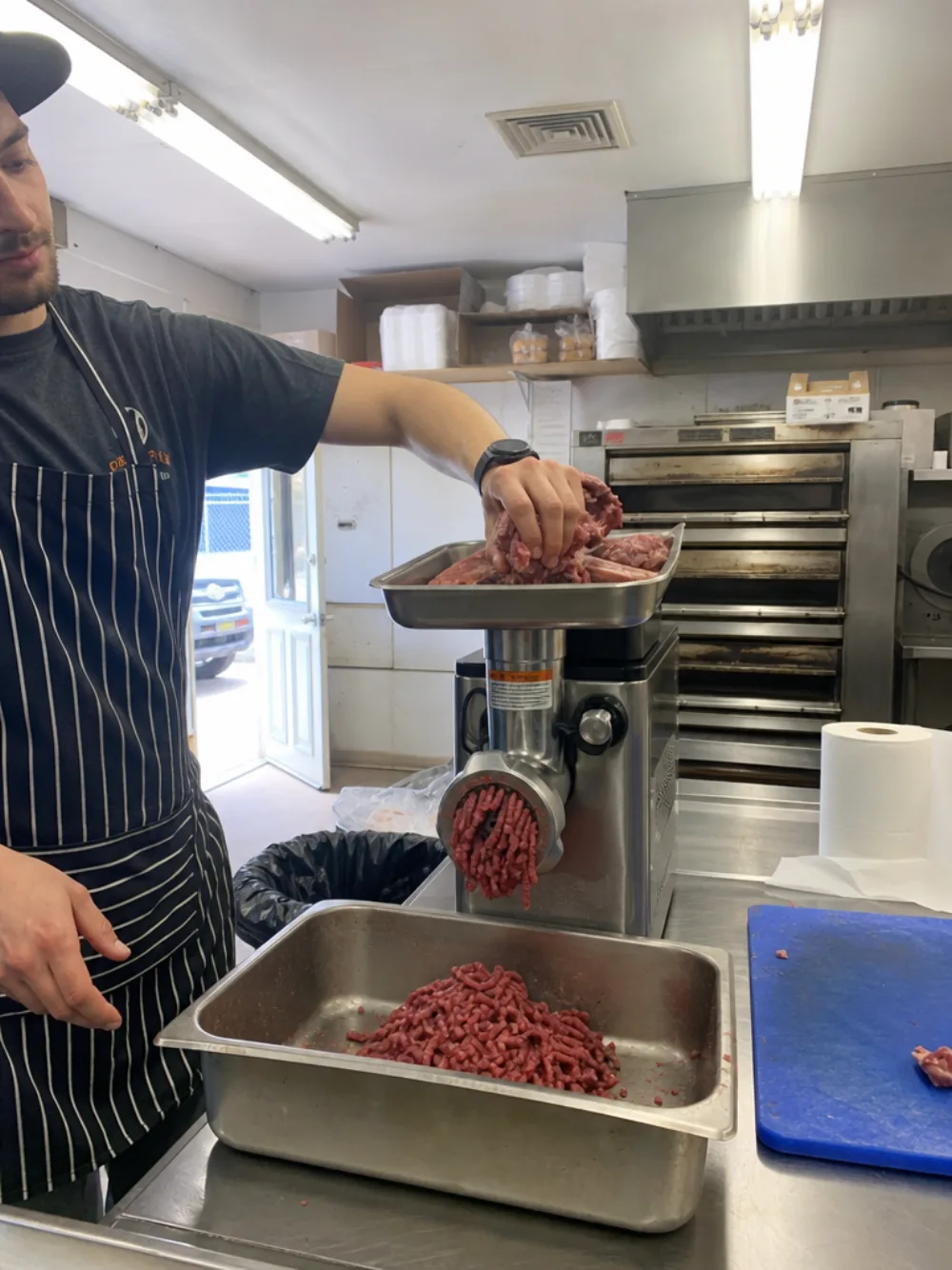 A cook feeding beef into the countertop grinder on the prep table