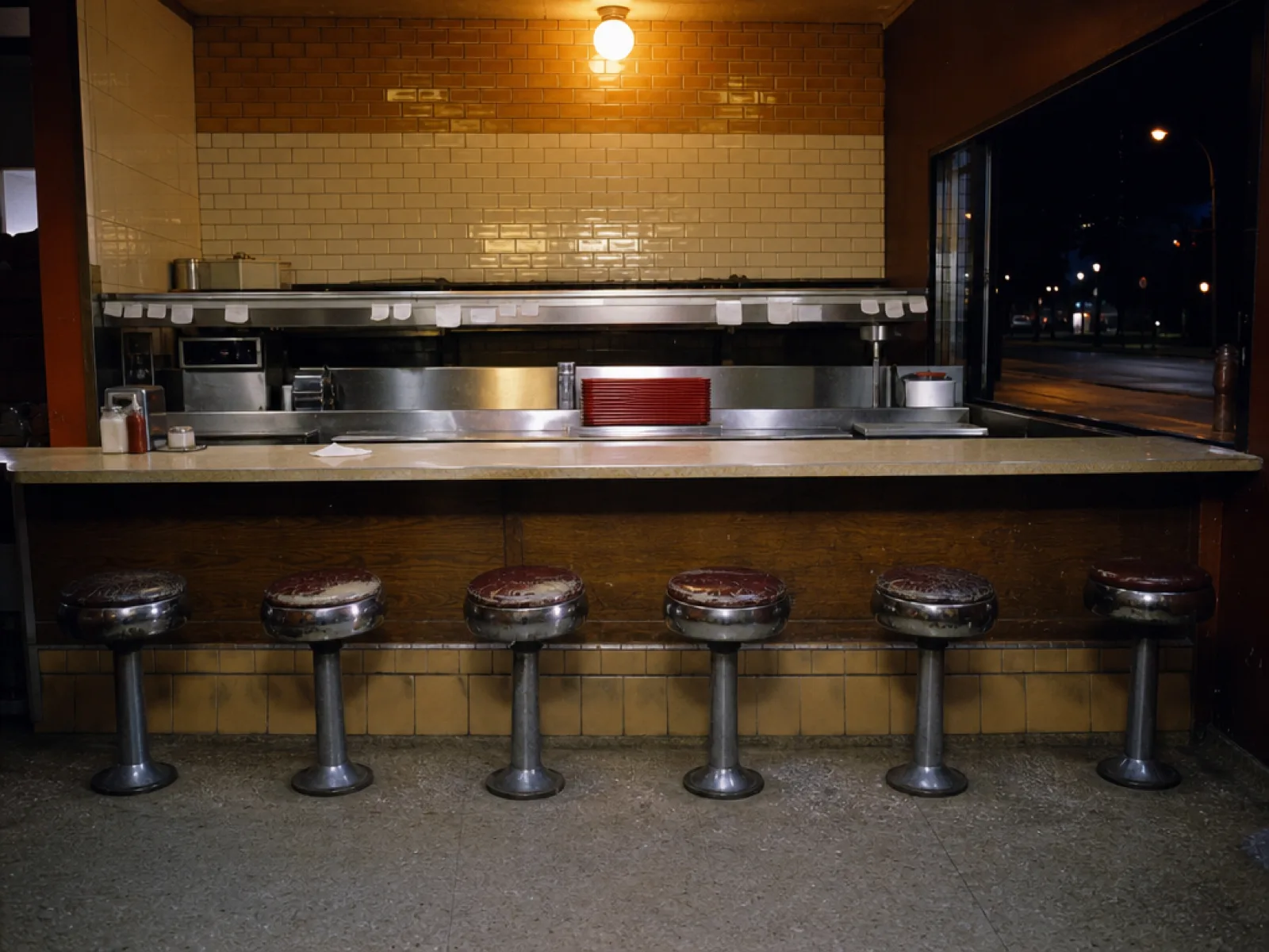 The empty counter and stools after close, street dark through the window