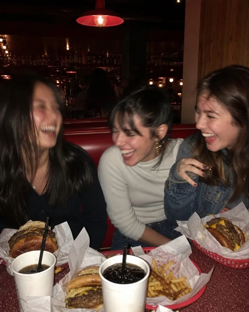 Three friends laughing over burgers, fries and sodas in a red diner booth