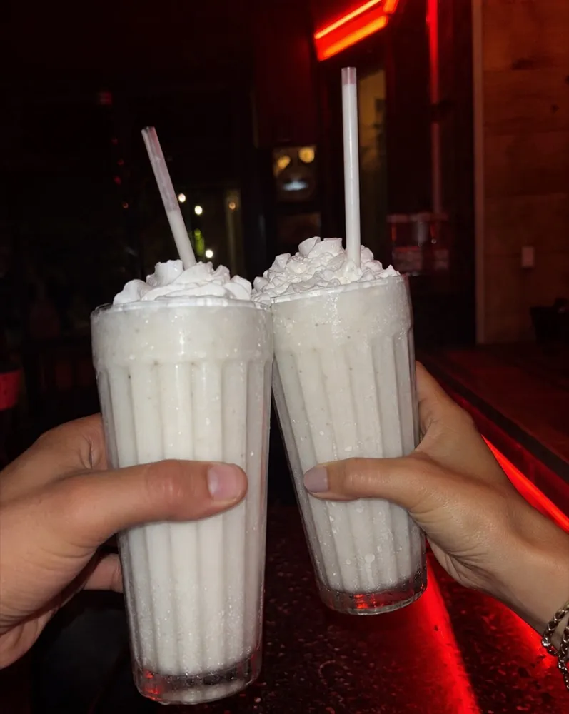 Two hands touching tall vanilla shakes together under neon