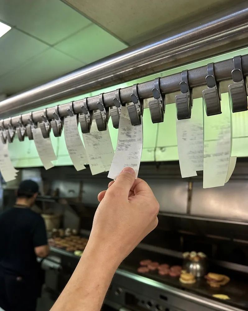 Paper tickets clipped in a row on the rail above the flat-top