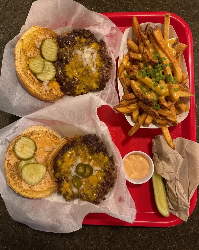 A red tray with two smash burgers and loaded fries