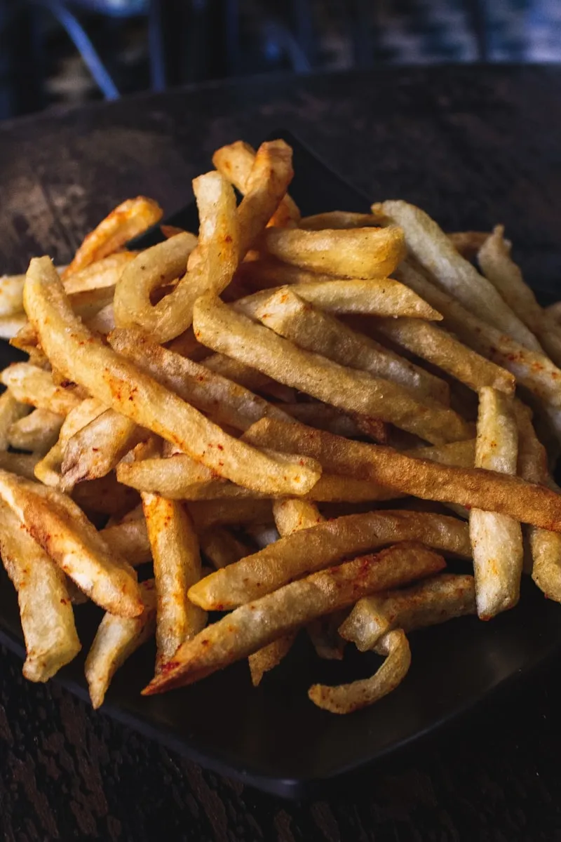 Pile of crispy hand-cut fries on a black plate