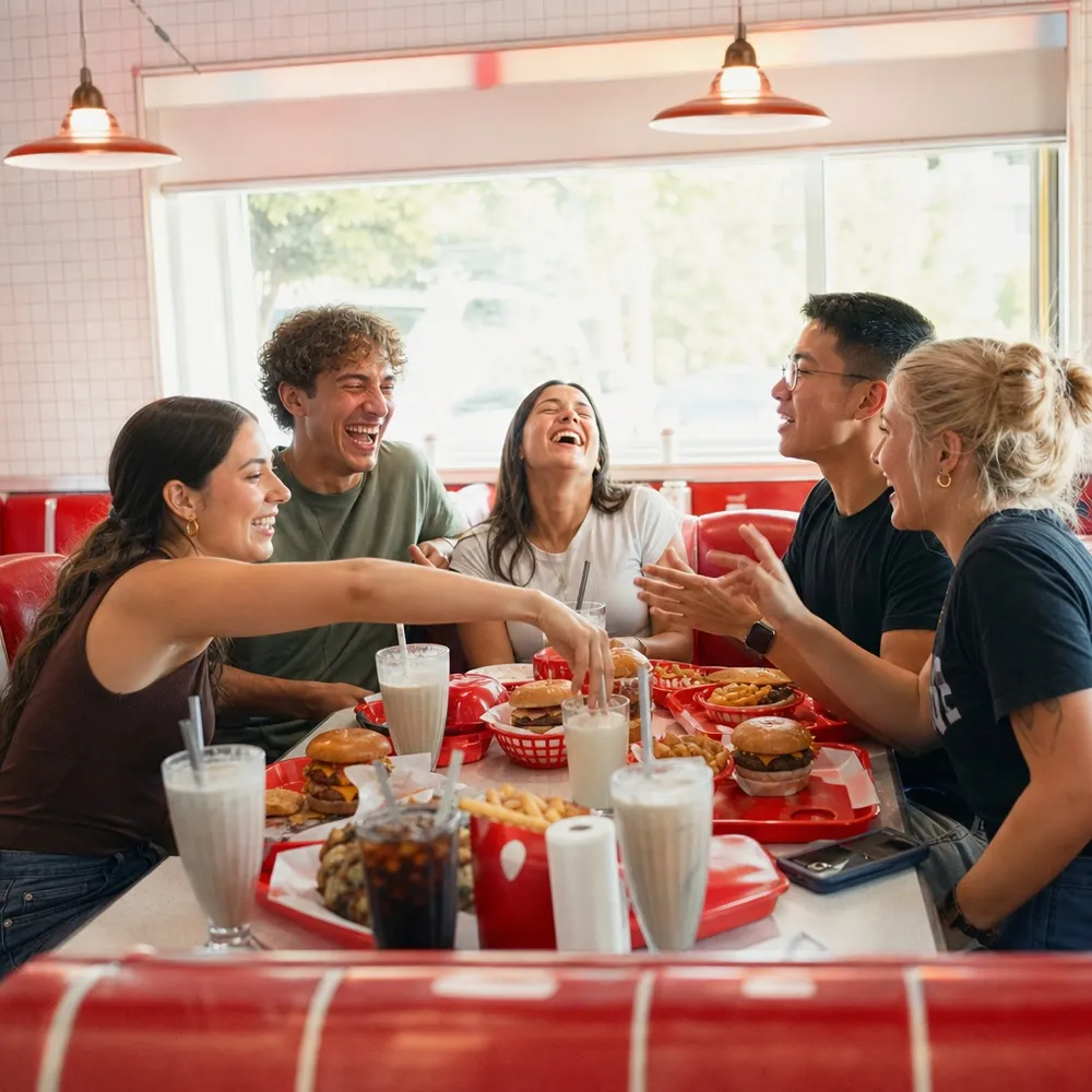 Five friends laughing over a table of burgers, fries and shakes